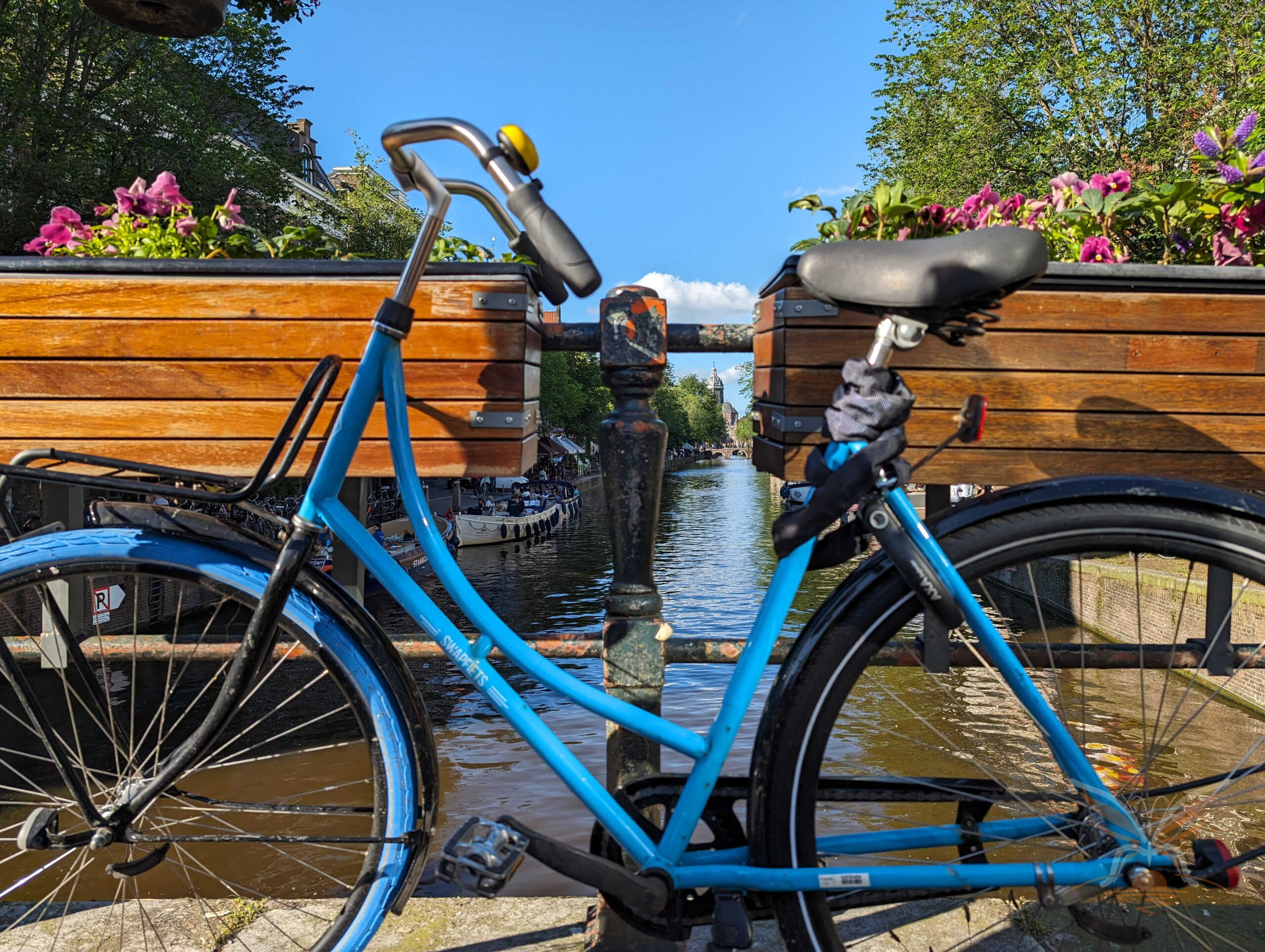Blue bicycle beside an Amsterdam canal, with colourful flowers along the bridge.