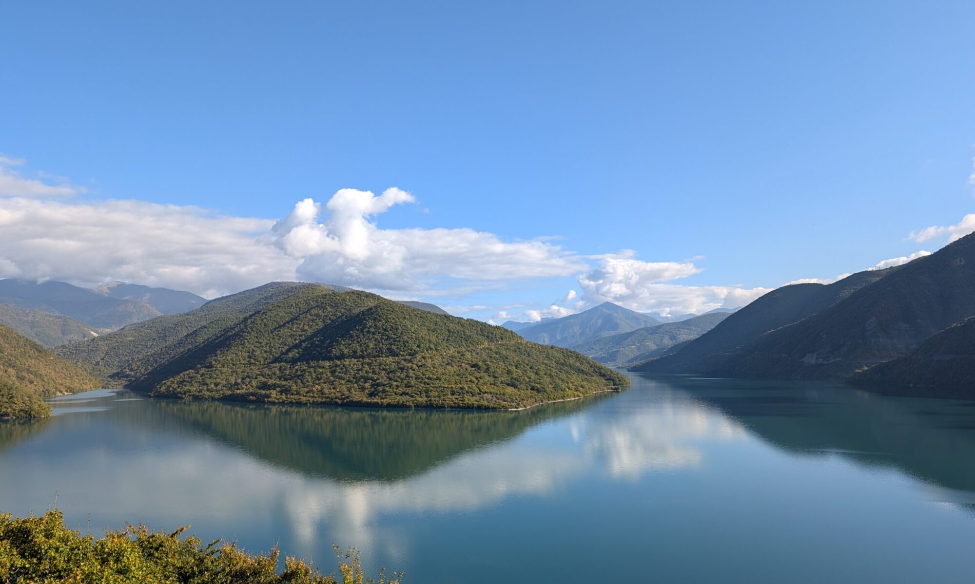 Calm mountain reservoir reflecting the surrounding hills and blue sky in Georgia.