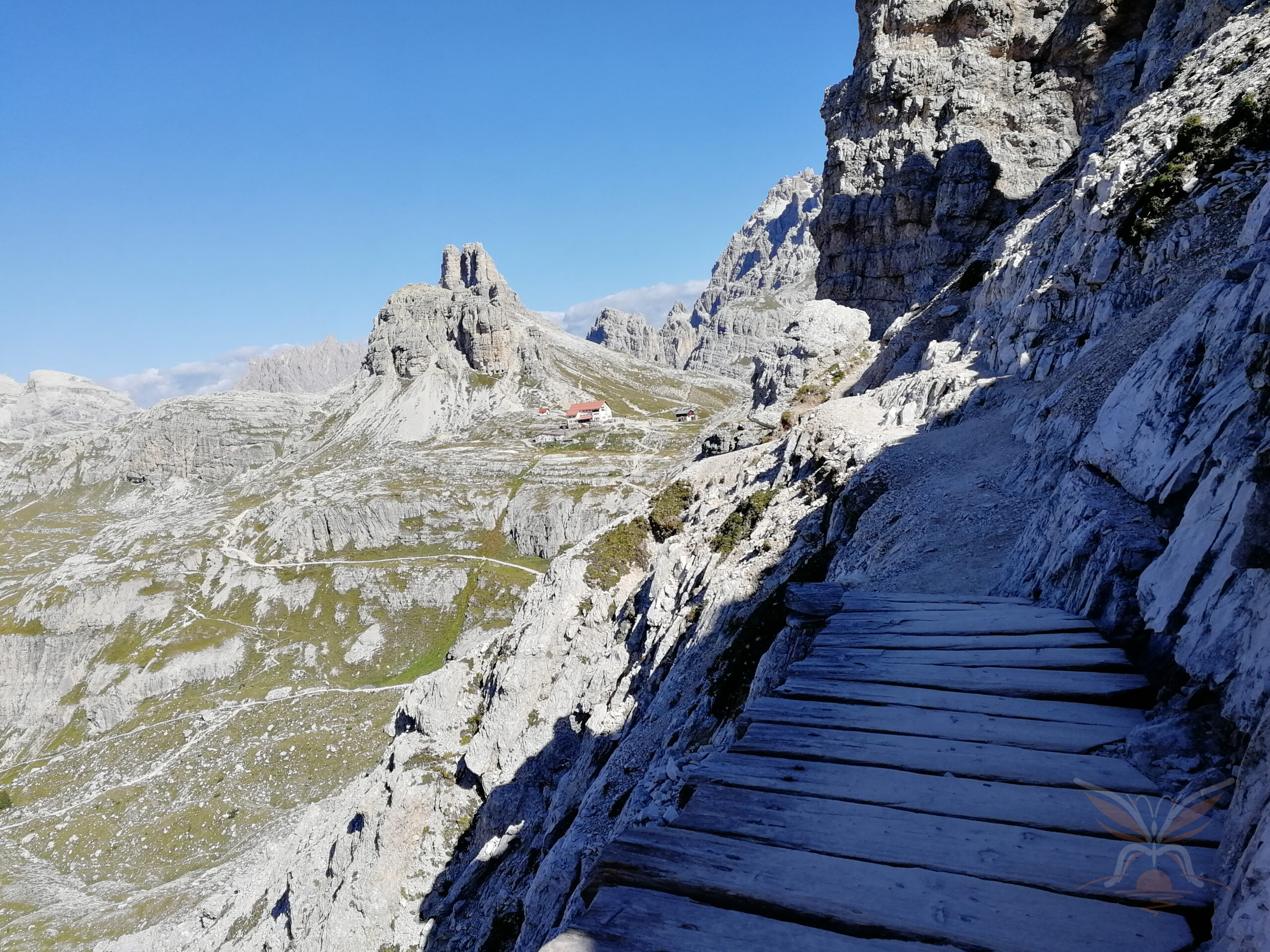 Rocky mountain path overlooking dramatic Dolomite peaks and a distant alpine refuge - Rifugio Locatelli.