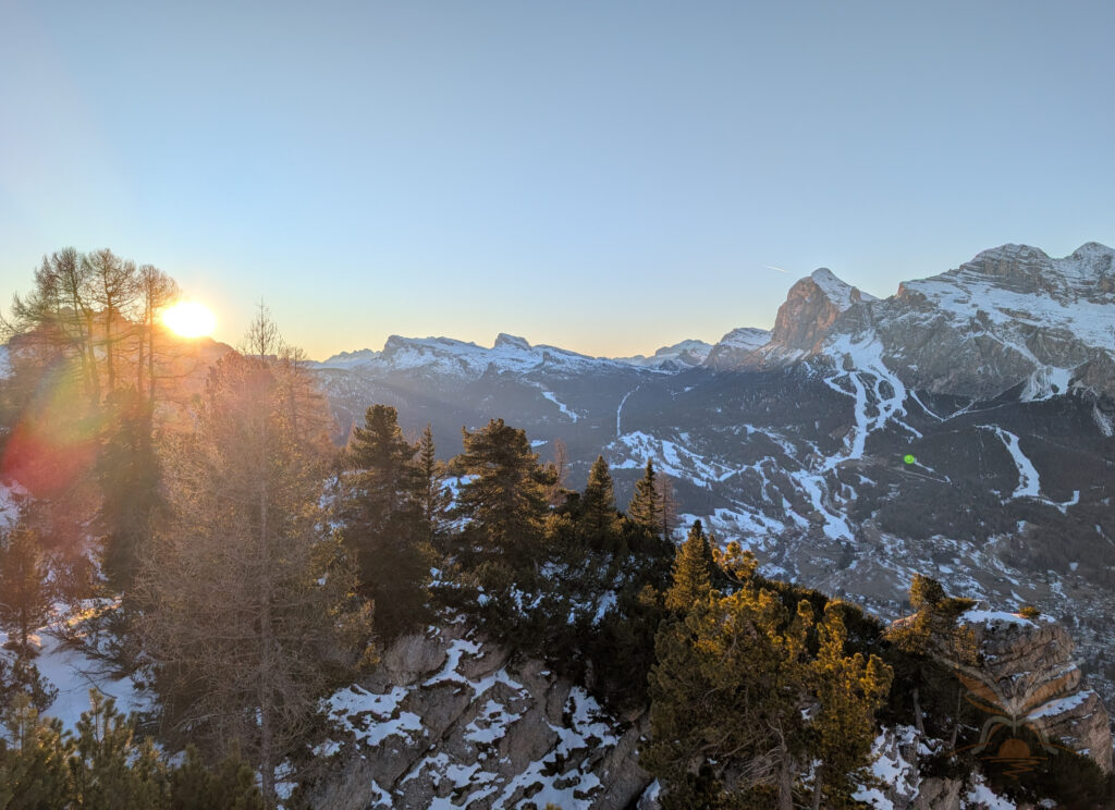 Sunlight breaking through trees above snow-covered peaks in the Dolomites, Italy.