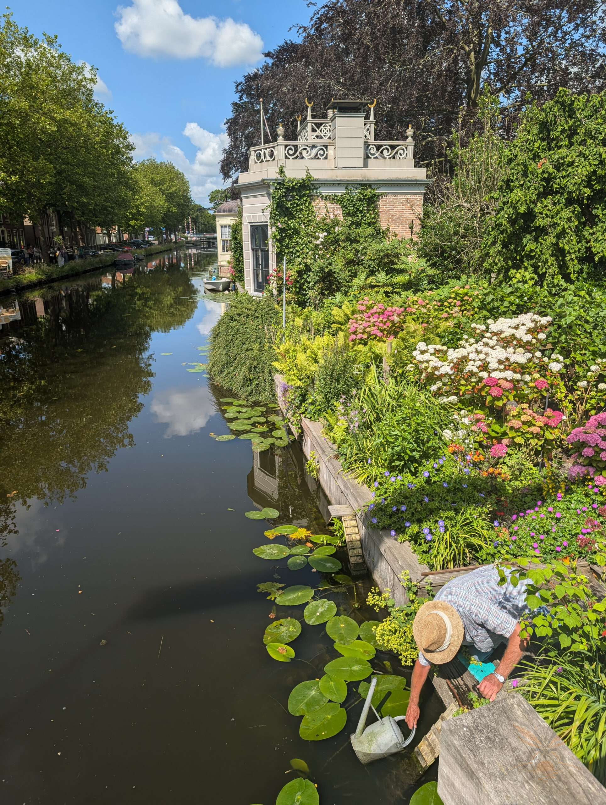 A person tending a flower-filled canal garden with water lilies in Giethoorn, Netherlands.