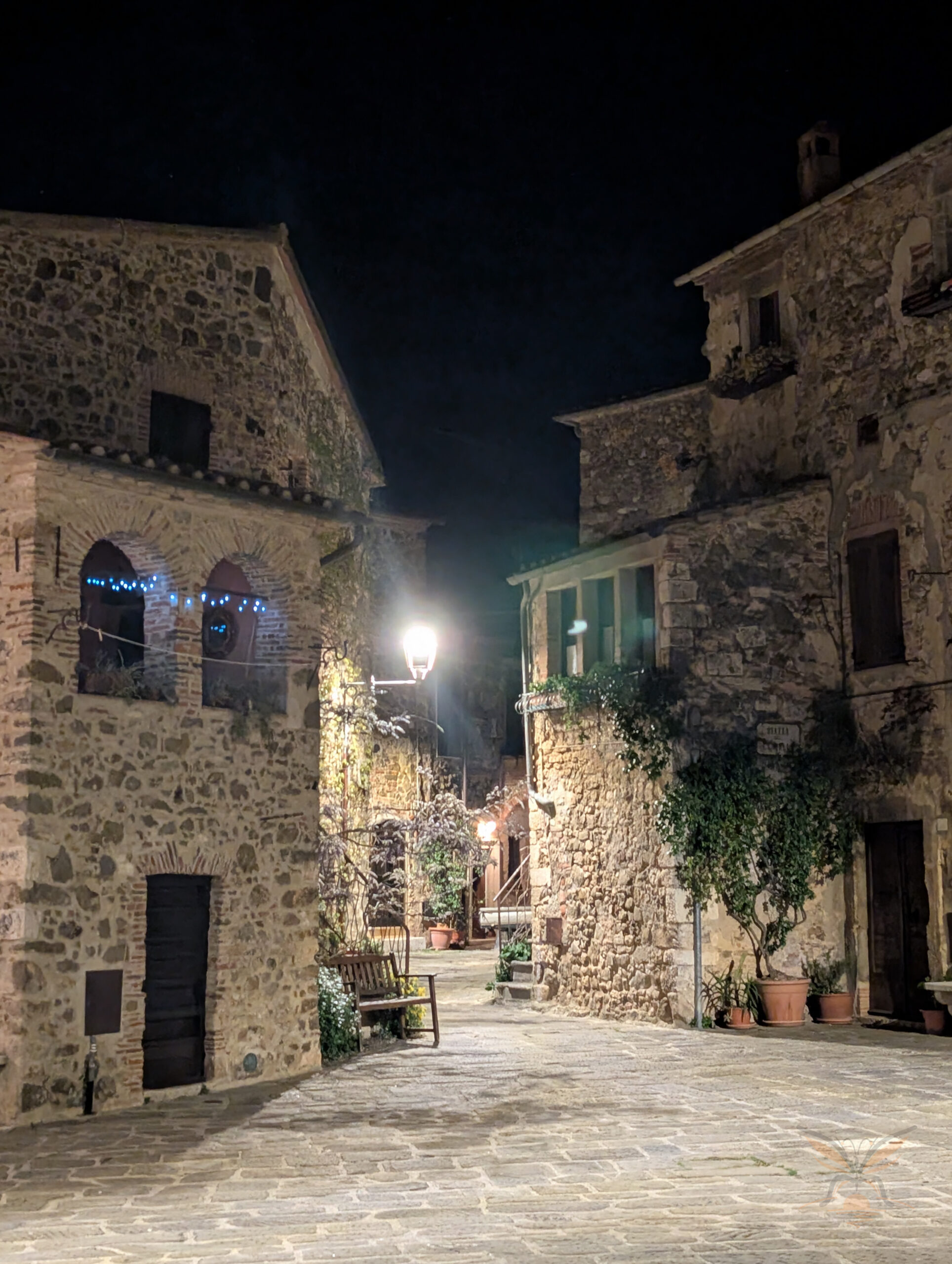 Stone houses and a quiet paved lane in the medieval village of Montemerano at night.