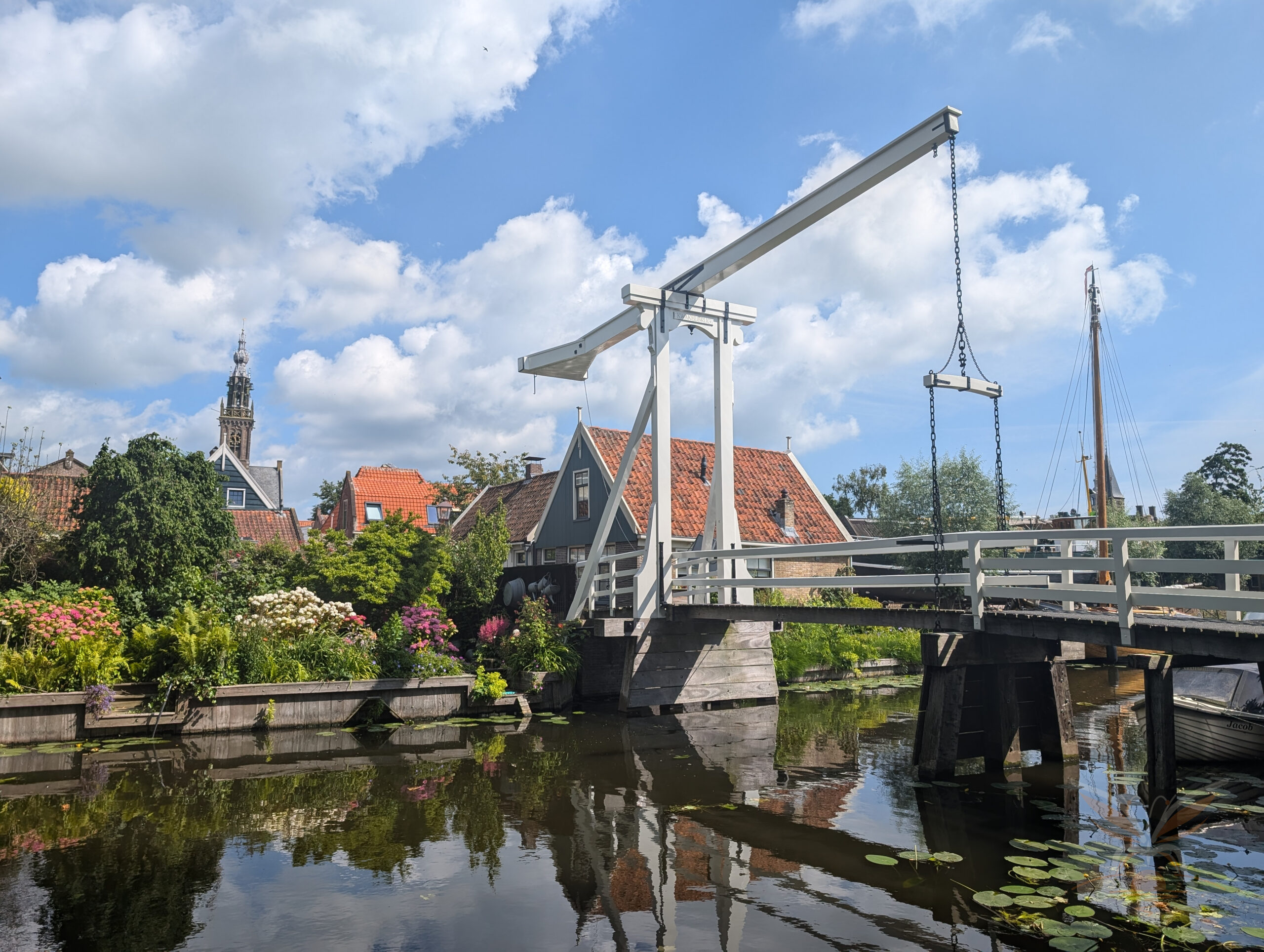 White wooden Kwakelbrug drawbridge over a canal in Edam, with traditional houses and a church tower in the background.
