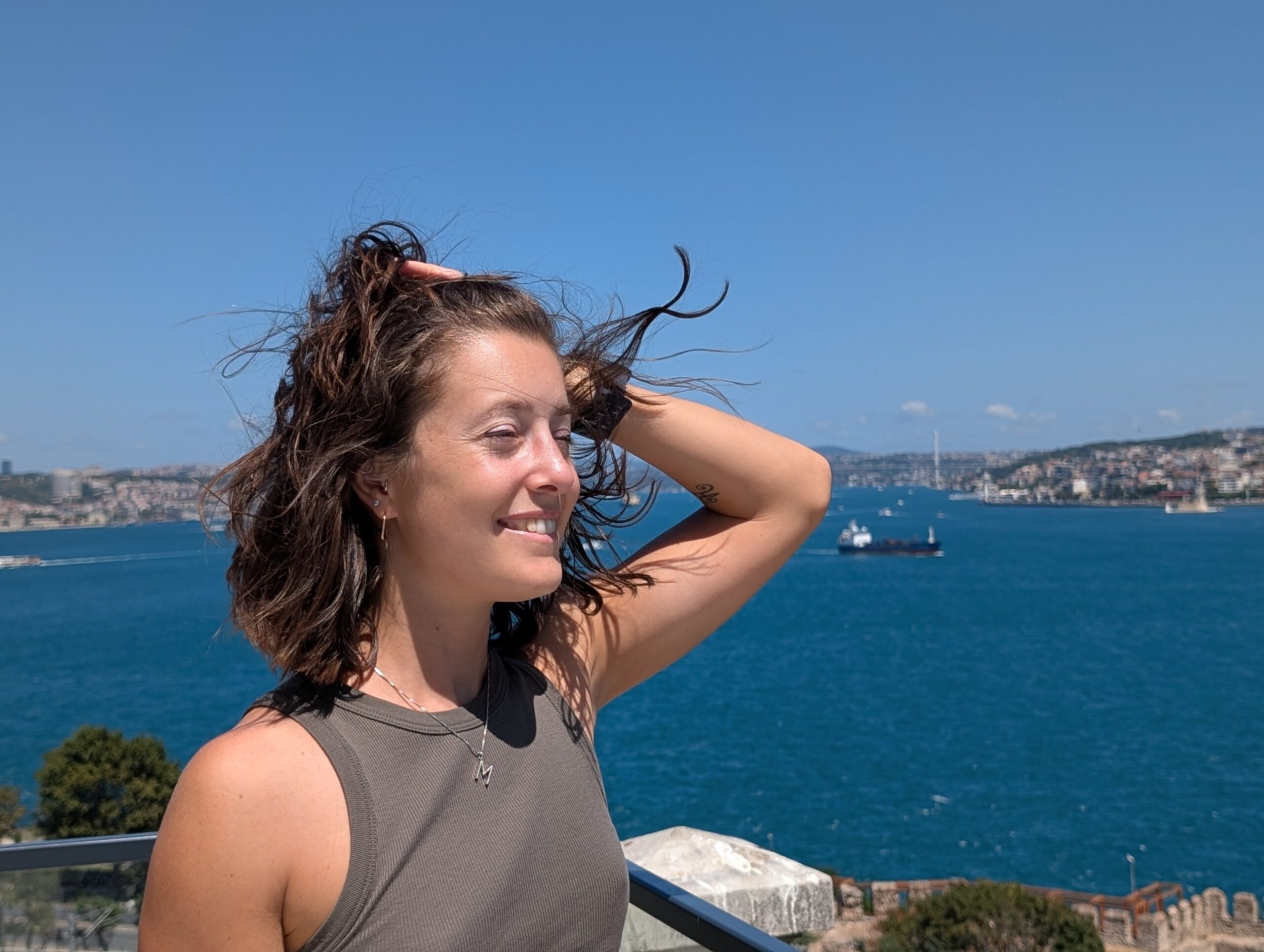 Mariachiara smiling in the wind with blue water and the Istanbul shoreline behind her.