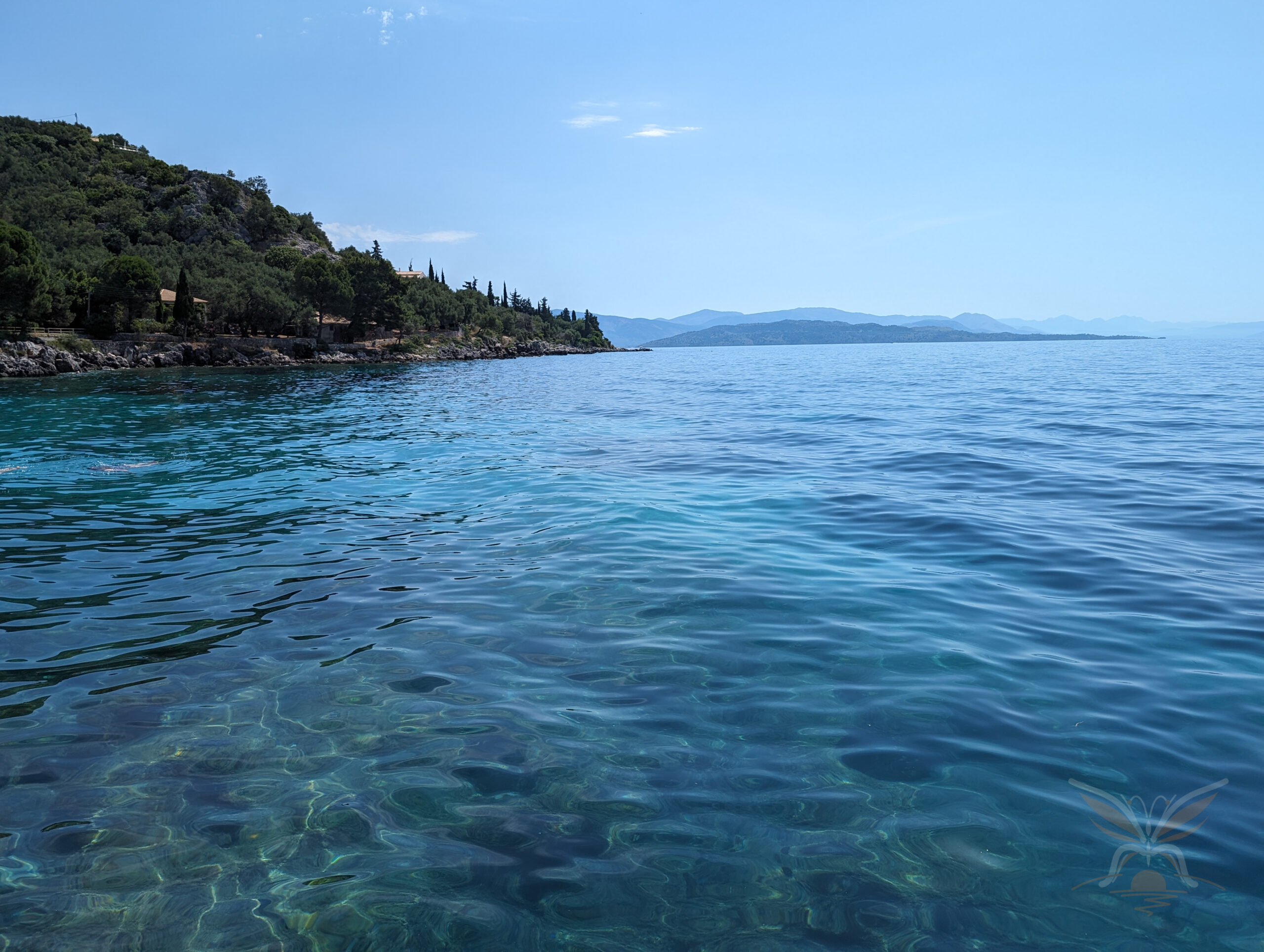 Clear blue Ionian Sea stretching beyond a rocky and wooded shoreline in north-eastern Corfu.