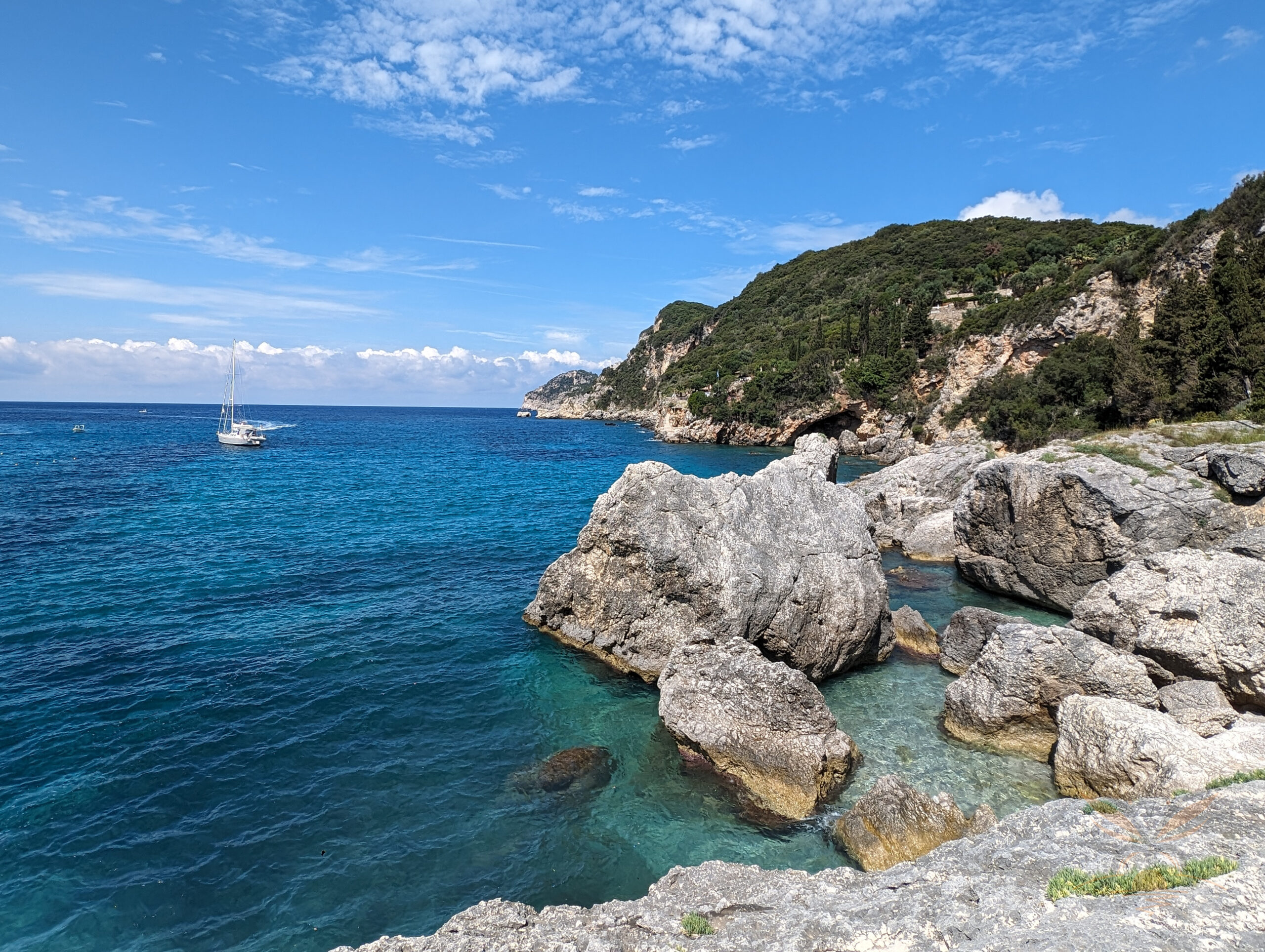 Pale rocks surrounding clear blue water in a secluded cove in Liapades Beach near Paleokastritsa, Corfu.
