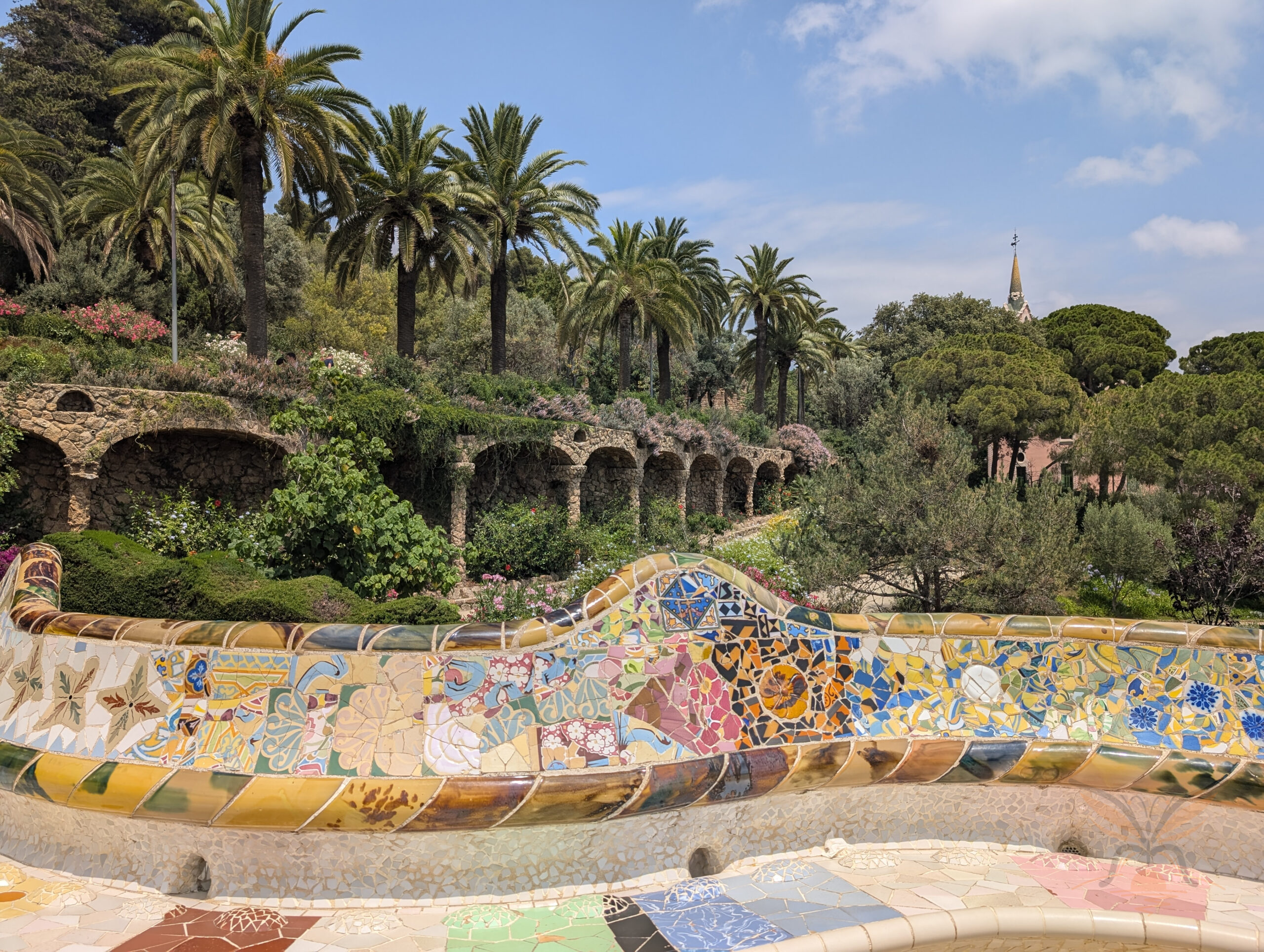 Colourful mosaic bench overlooking palm trees and gardens in Park Güell, Barcelona.