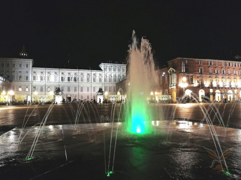 Illuminated fountains in Piazza Castello with the Royal Palace of Turin in the background at night.