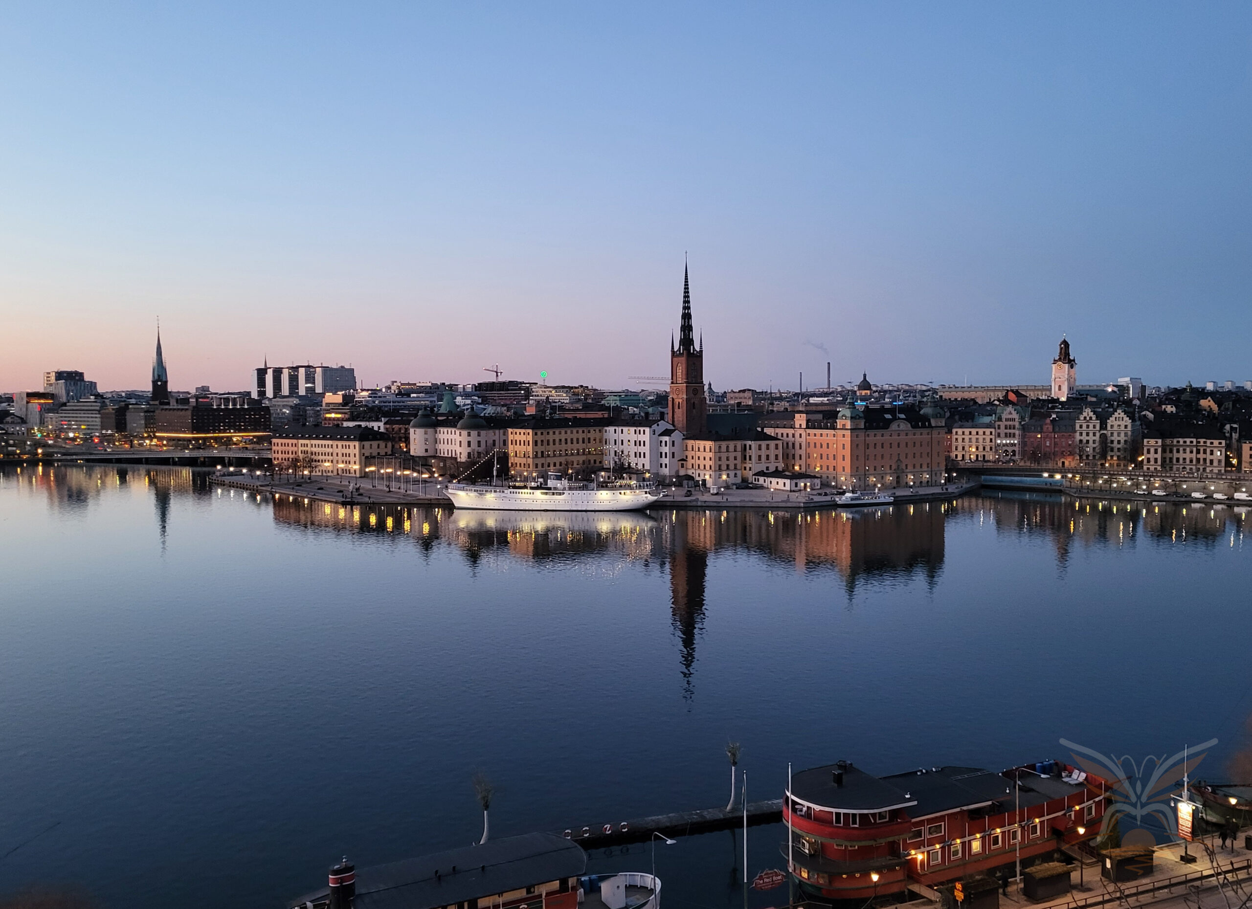 Riddarholmen skyline and church spire reflected in calm water at blue hour in Stockholm.