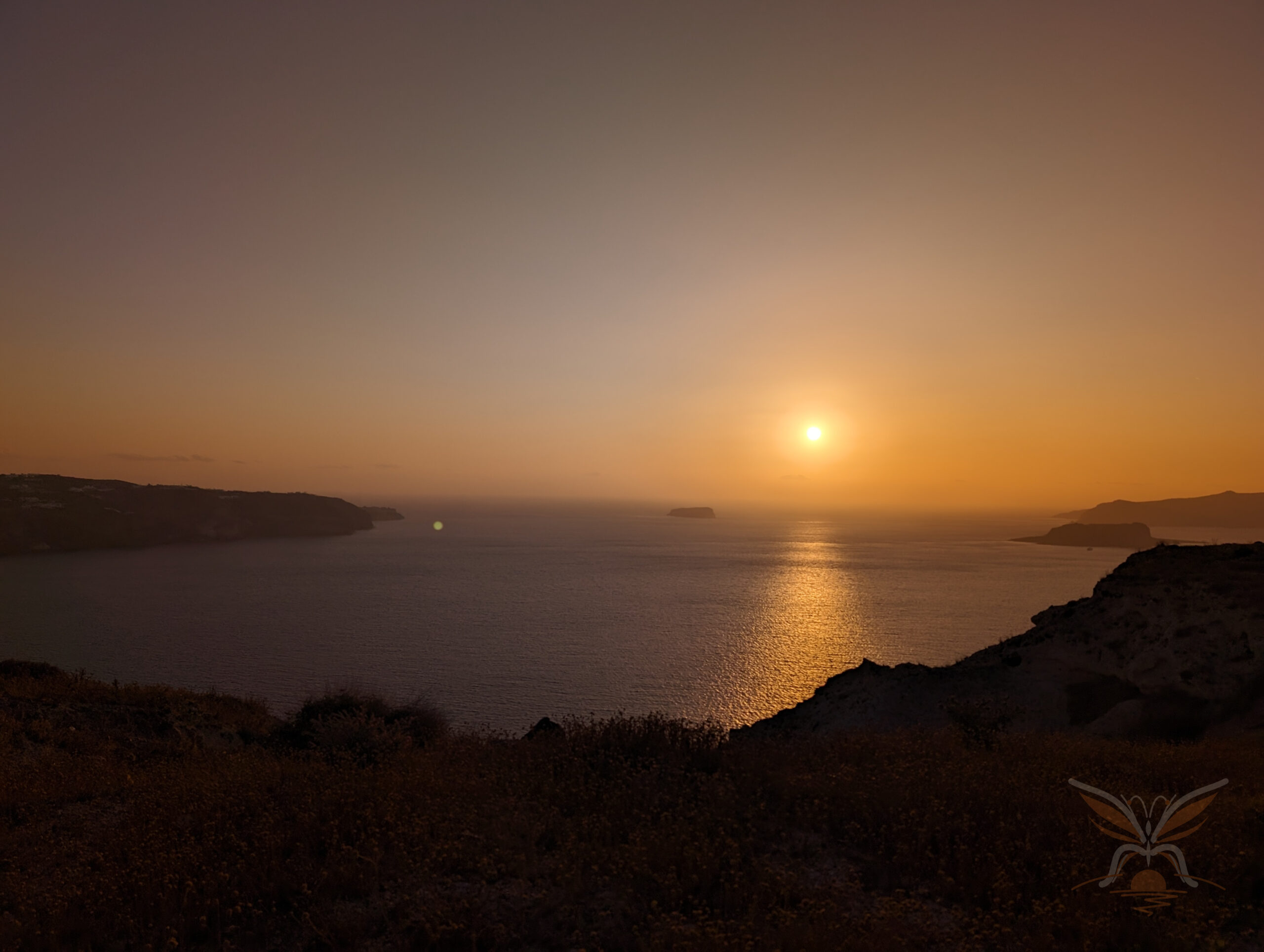 Golden sun setting over the Aegean Sea beside the dark coastline of Santorini.