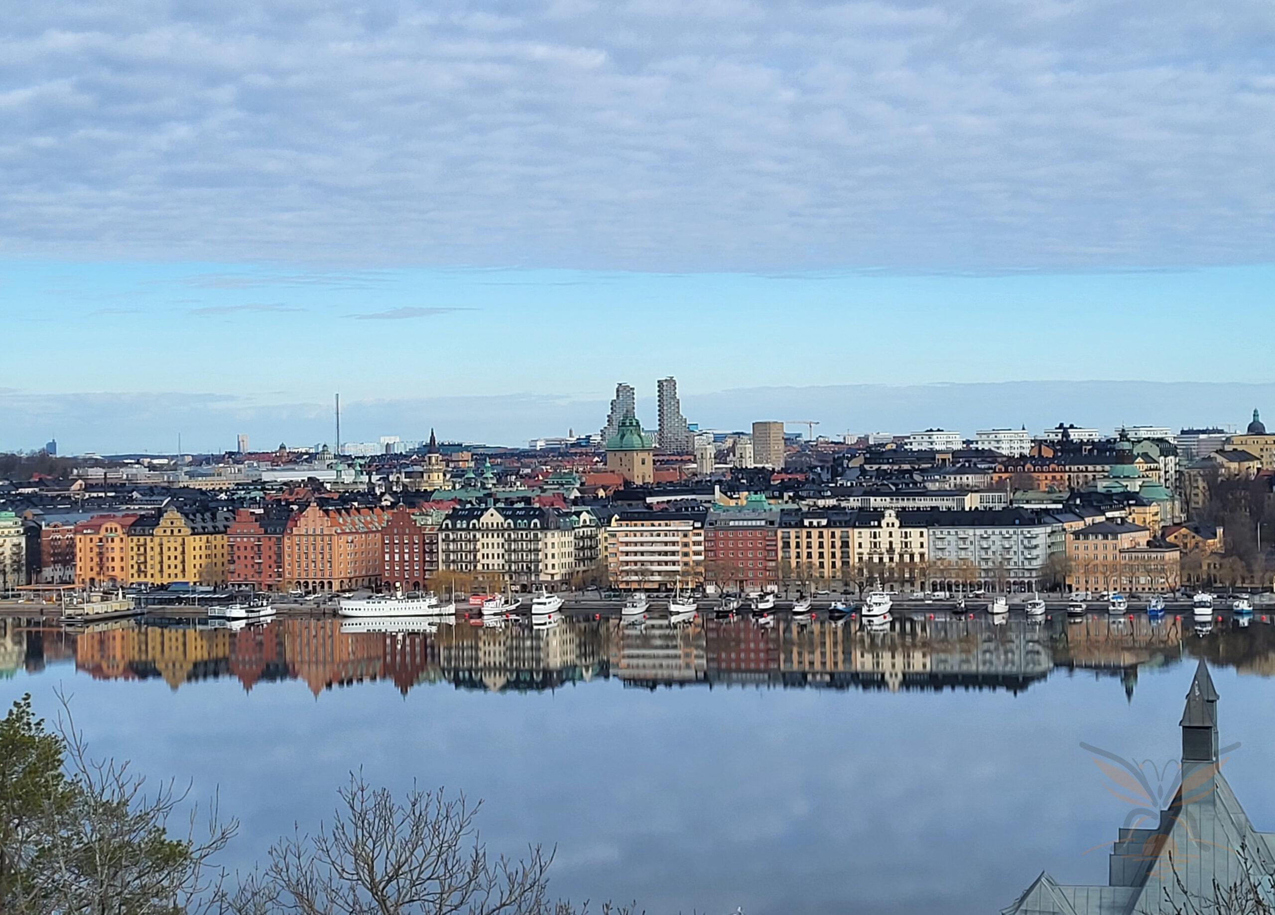 Panoramic view across the Stockholm waterfront towards Gamla Stan under a pale blue sky.
