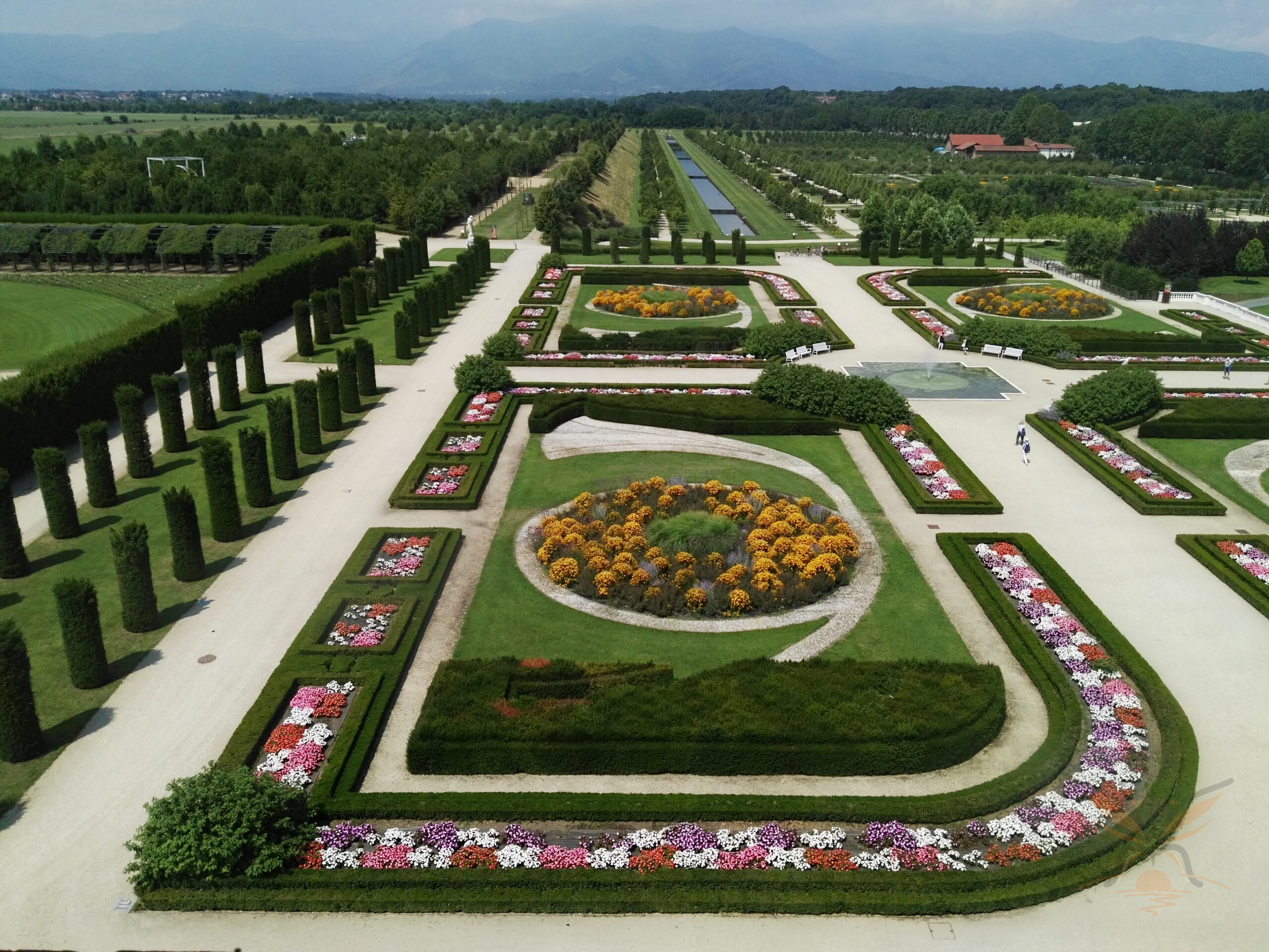 Formal gardens at Venaria Reale with clipped trees, flowerbeds and distant mountains.