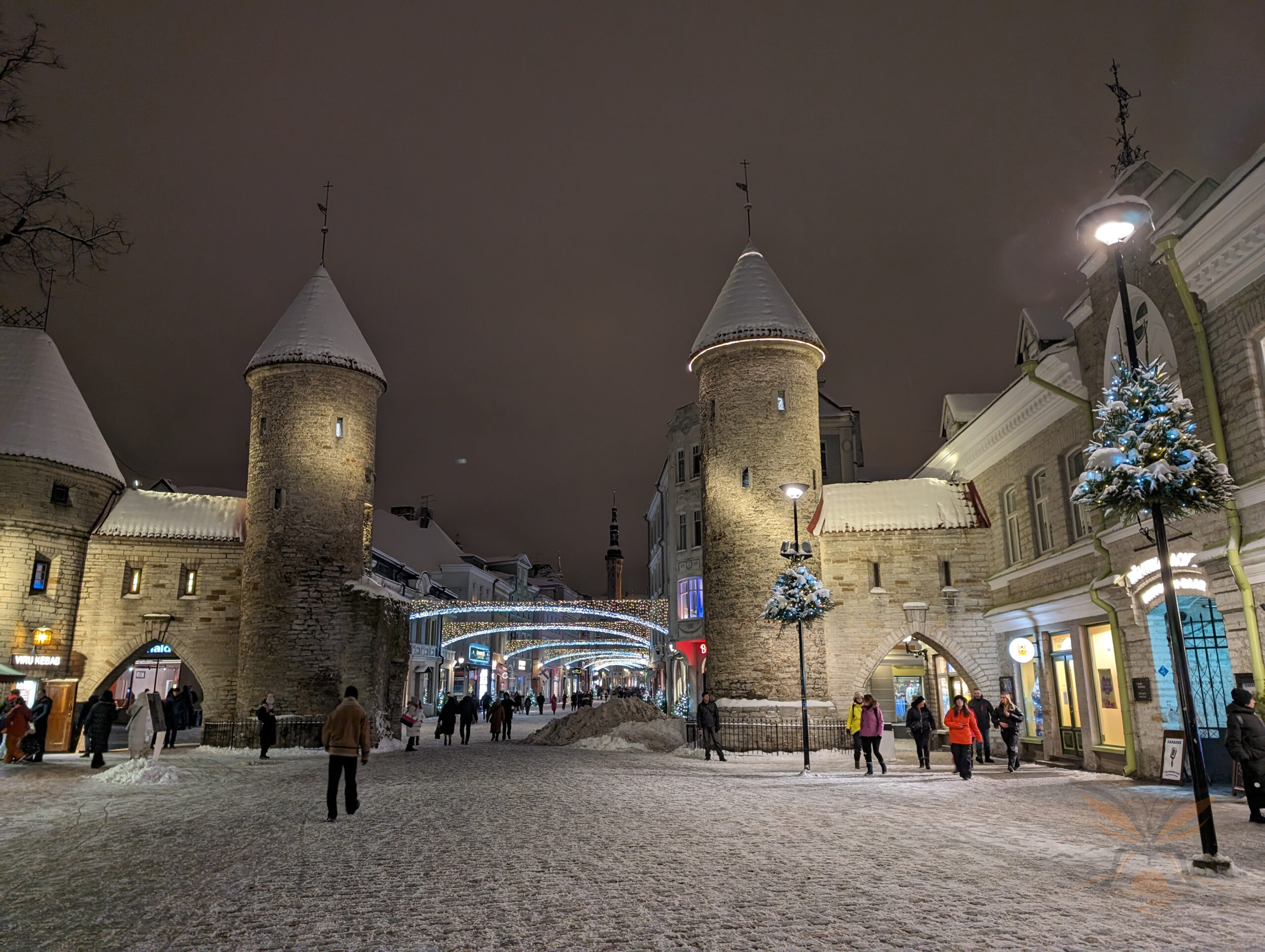 Snow-covered street leading through the illuminated Viru Gate in Tallinn at night.